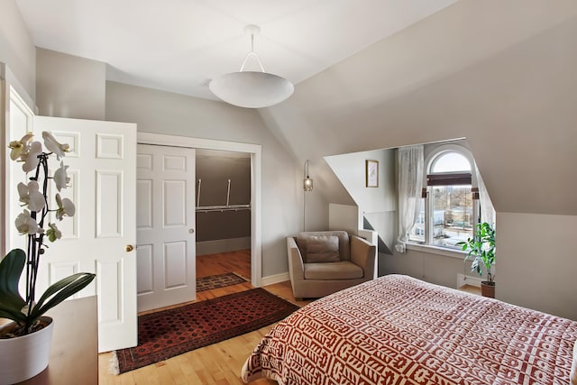 bedroom featuring vaulted ceiling, wood finished floors, a closet, and baseboards