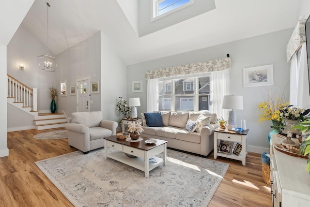 living area featuring stairs, a high ceiling, light wood-style floors, and baseboards