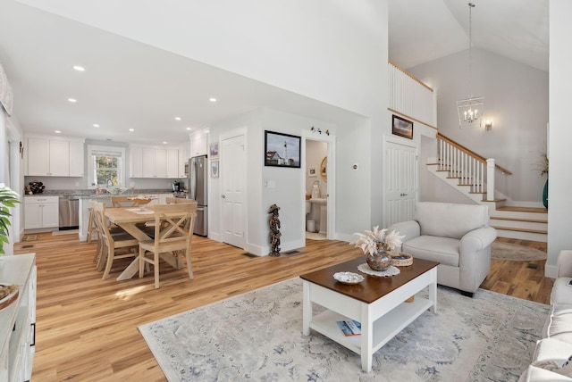 living room featuring stairway, recessed lighting, an inviting chandelier, light wood-style floors, and high vaulted ceiling