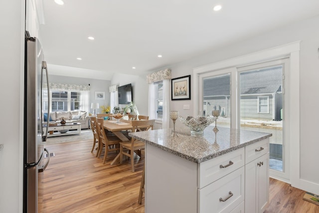 kitchen with light stone counters, light wood-style flooring, freestanding refrigerator, white cabinetry, and a center island