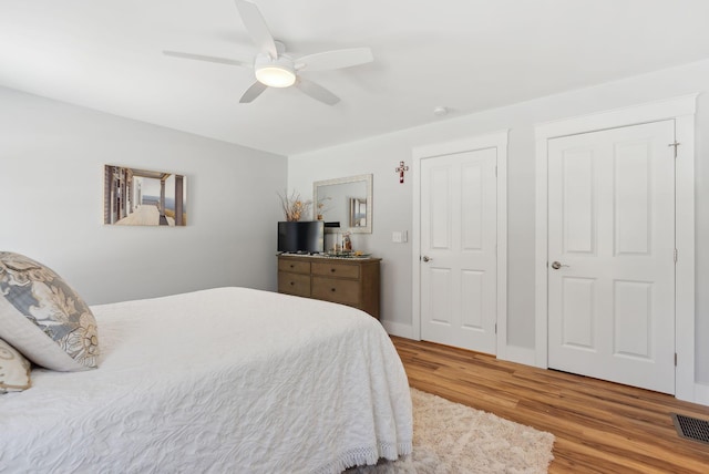 bedroom featuring ceiling fan, visible vents, baseboards, and wood finished floors