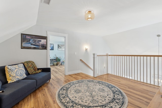 living area with visible vents, baseboards, light wood-style floors, and vaulted ceiling