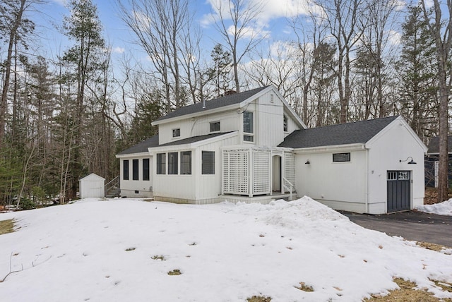 snow covered property featuring a shed, a garage, a shingled roof, and an outdoor structure