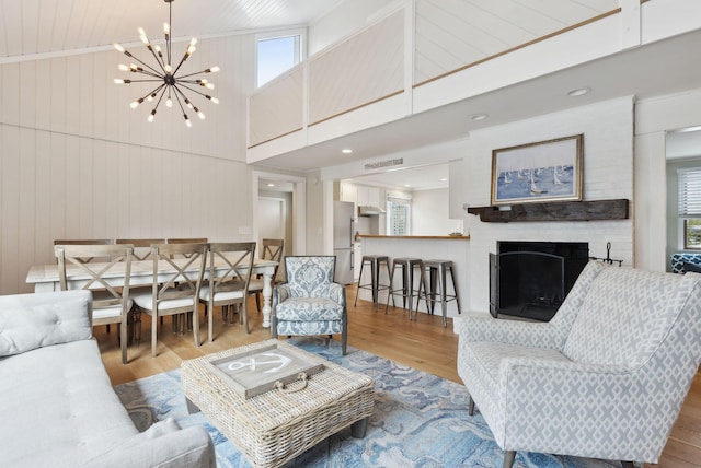 living room featuring wood finished floors, an inviting chandelier, wood walls, a brick fireplace, and vaulted ceiling