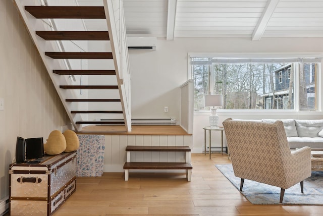 sitting room with stairs, beam ceiling, baseboard heating, a wall mounted AC, and wood-type flooring