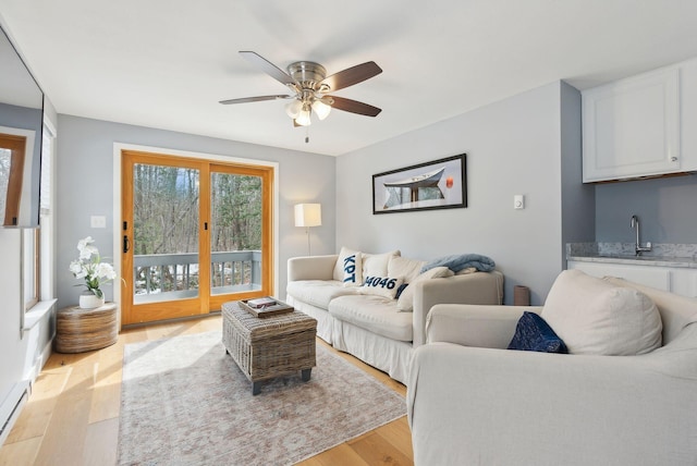 living room with indoor wet bar, baseboard heating, a ceiling fan, and light wood finished floors