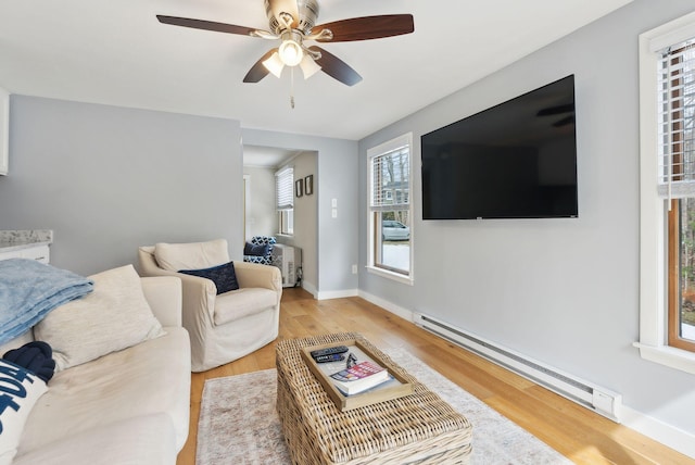 living area featuring a baseboard radiator, baseboards, light wood-style floors, and a ceiling fan