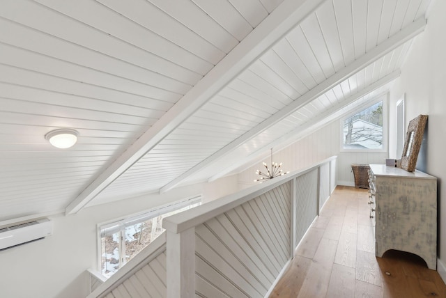 hall featuring a wall mounted air conditioner, beam ceiling, an upstairs landing, light wood-style floors, and an inviting chandelier