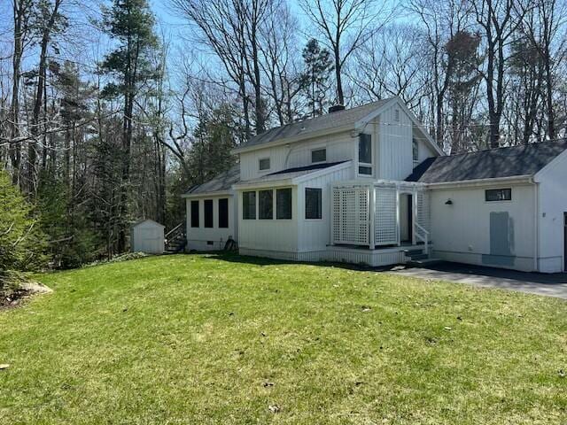 back of property featuring a storage shed, a yard, an outbuilding, and roof with shingles