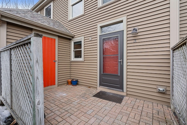 entrance to property with a patio area and a shingled roof