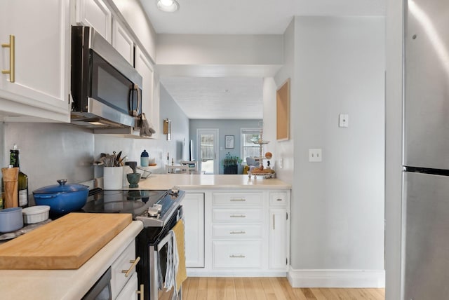 kitchen with light wood-type flooring, stainless steel appliances, white cabinetry, and light countertops