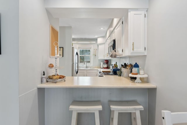 kitchen featuring a breakfast bar, a peninsula, a sink, appliances with stainless steel finishes, and white cabinetry