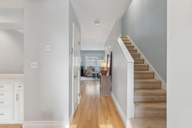 corridor with baseboards, stairs, and light wood-style floors