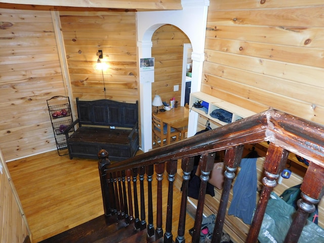 staircase with arched walkways, wooden walls, and wood finished floors