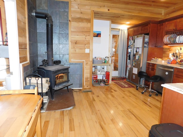 kitchen with light wood finished floors, stainless steel appliances, light countertops, wood ceiling, and a wood stove