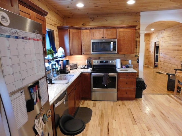 kitchen featuring wooden walls, stainless steel appliances, light countertops, and a sink