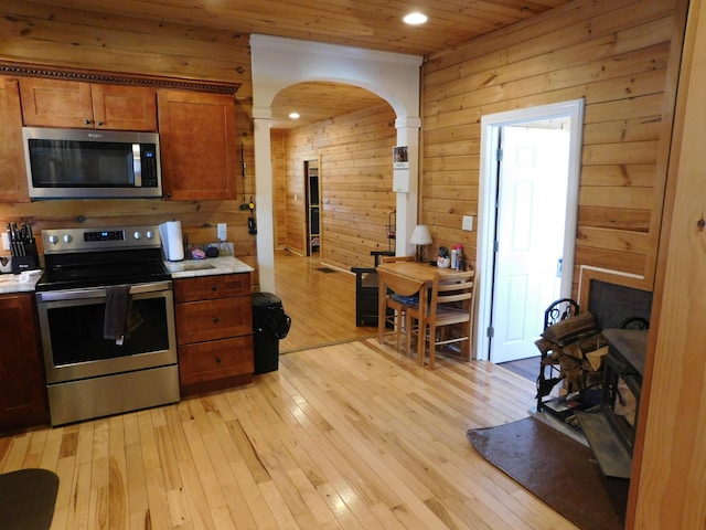 kitchen featuring light wood finished floors, wood walls, light countertops, brown cabinets, and stainless steel appliances