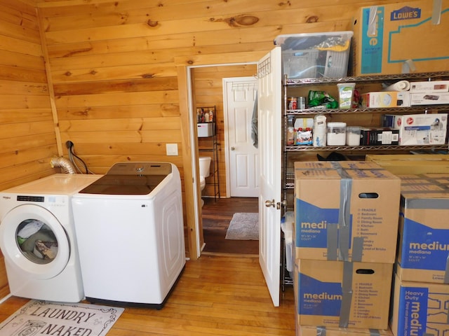 washroom with laundry area, washing machine and dryer, light wood-style flooring, and wood walls