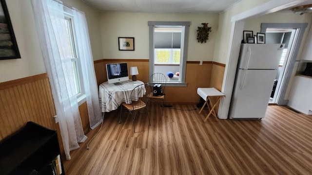 bedroom with a wainscoted wall, wood finished floors, wood walls, and freestanding refrigerator