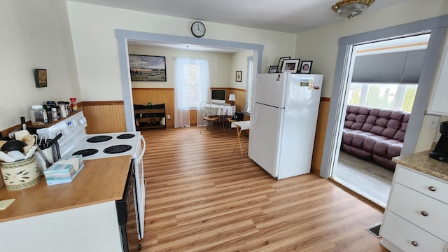 kitchen featuring white appliances, plenty of natural light, light wood-style floors, and a wainscoted wall