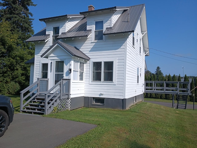 view of front facade featuring a chimney, a front yard, and metal roof