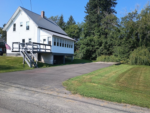 view of side of property featuring a deck, a yard, stairway, metal roof, and a chimney