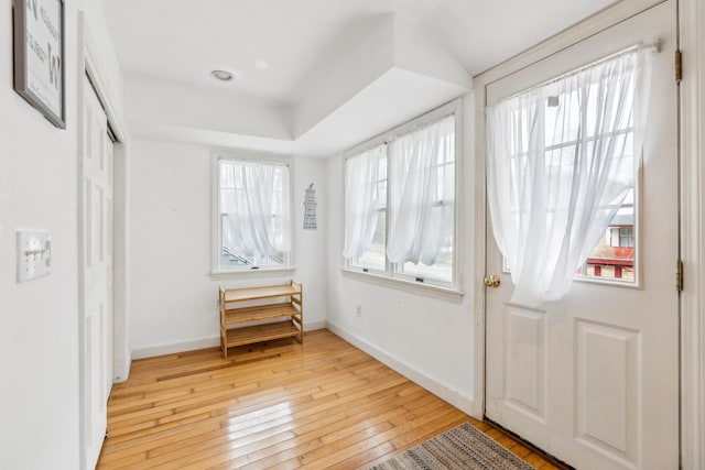 entryway with a raised ceiling, light wood-style floors, and baseboards