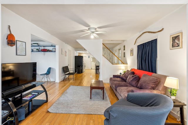 living area featuring stairway, baseboards, ceiling fan, and light wood finished floors