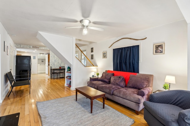 living room with stairs, a ceiling fan, baseboards, and light wood finished floors