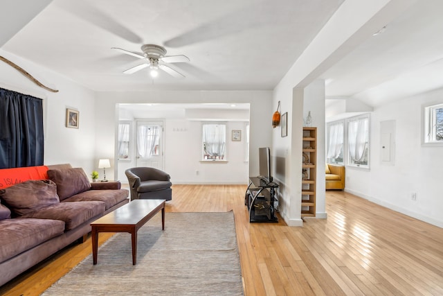 living area featuring electric panel, baseboards, a ceiling fan, and light wood finished floors