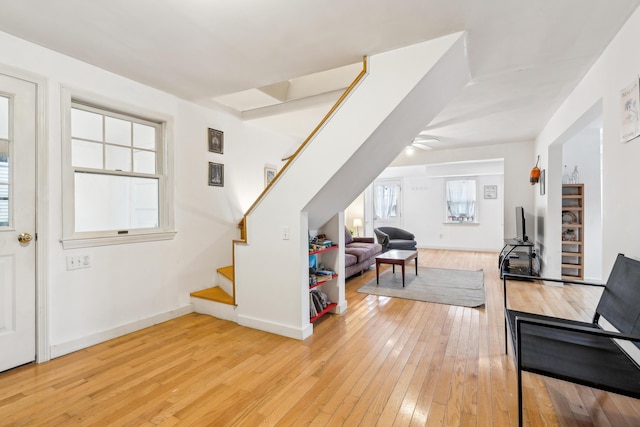 interior space featuring baseboards, a ceiling fan, light wood-style flooring, and stairs