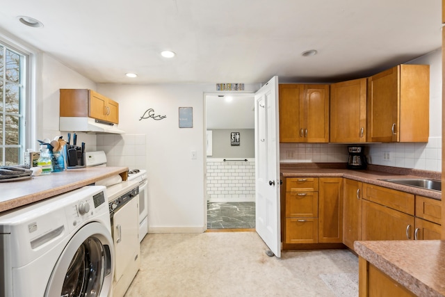 kitchen with washer / clothes dryer, a sink, decorative backsplash, under cabinet range hood, and brown cabinets