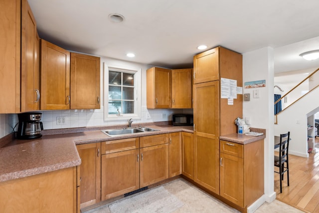 kitchen with a sink, brown cabinets, backsplash, and black microwave