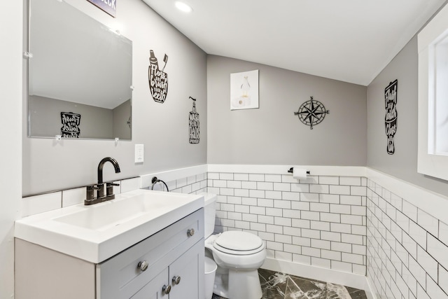 half bath featuring vanity, a wainscoted wall, tile walls, toilet, and marble finish floor