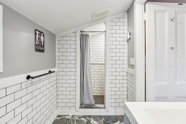 bathroom with marble finish floor, tile walls, a shower stall, and vaulted ceiling