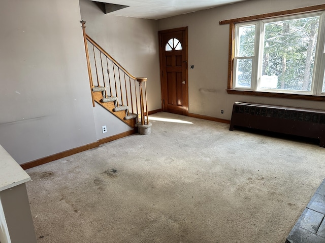 entrance foyer with baseboards, radiator, stairs, and carpet