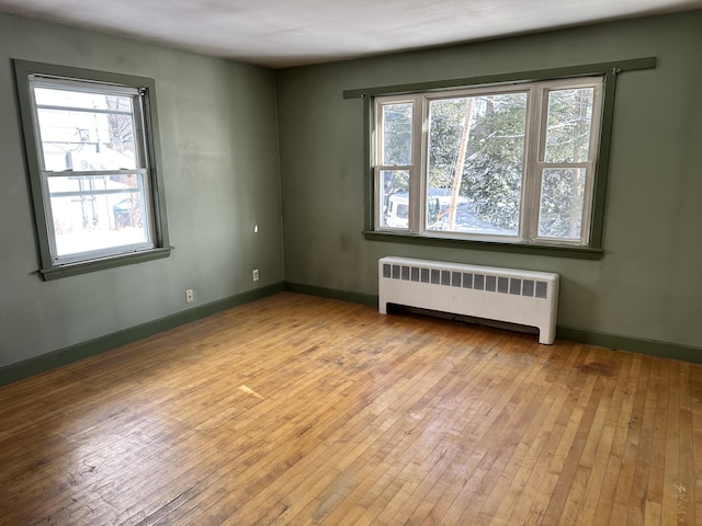 spare room featuring baseboards, wood-type flooring, radiator, and a healthy amount of sunlight