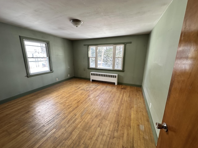 empty room featuring wood-type flooring, a healthy amount of sunlight, and radiator heating unit