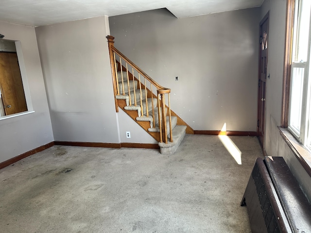 unfurnished living room with stairway, heating unit, carpet, and baseboards