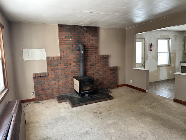 unfurnished living room featuring a wall unit AC, a wood stove, carpet flooring, and baseboards