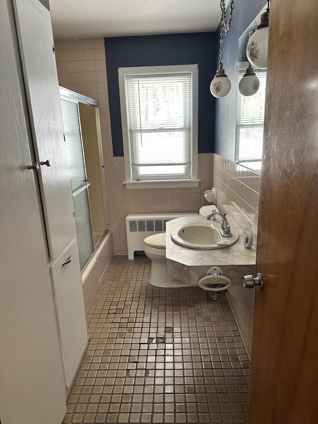 full bath featuring toilet, a sink, radiator heating unit, combined bath / shower with glass door, and tile walls