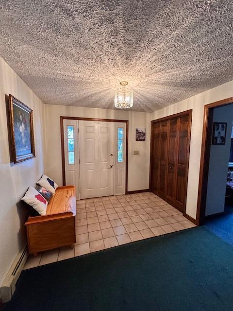 foyer entrance with light carpet, a textured ceiling, baseboard heating, light tile patterned floors, and an inviting chandelier