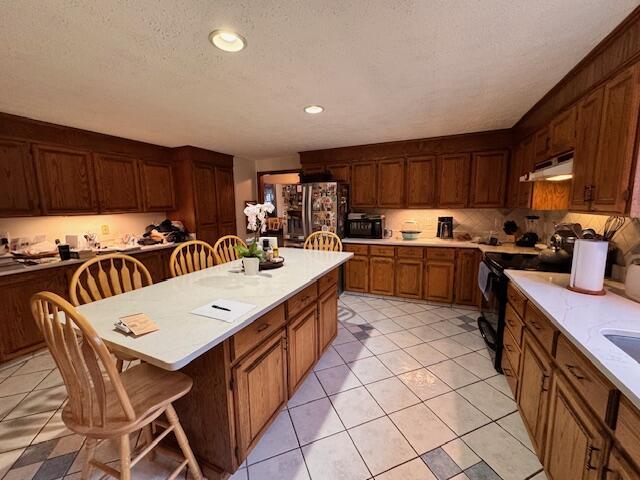 kitchen with light countertops, black range with electric stovetop, a kitchen island, under cabinet range hood, and freestanding refrigerator