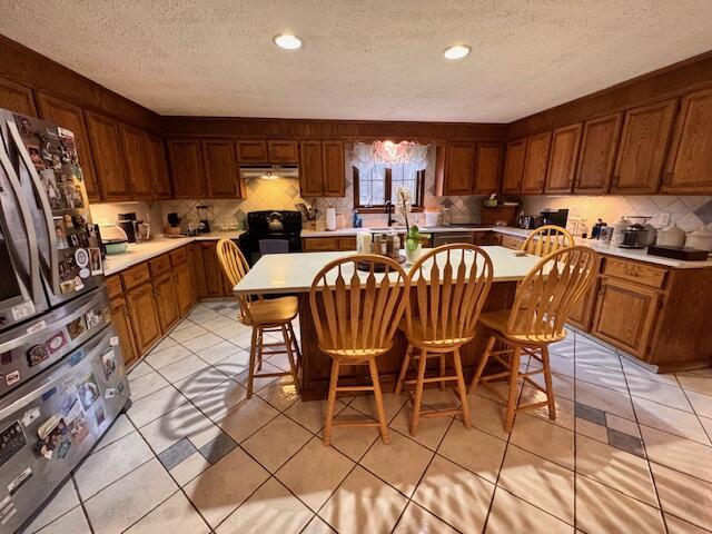 kitchen featuring light countertops, tasteful backsplash, under cabinet range hood, a kitchen island, and brown cabinetry