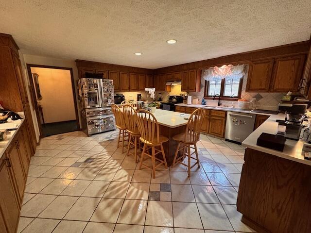 kitchen with light countertops, light tile patterned floors, stainless steel appliances, decorative backsplash, and a sink