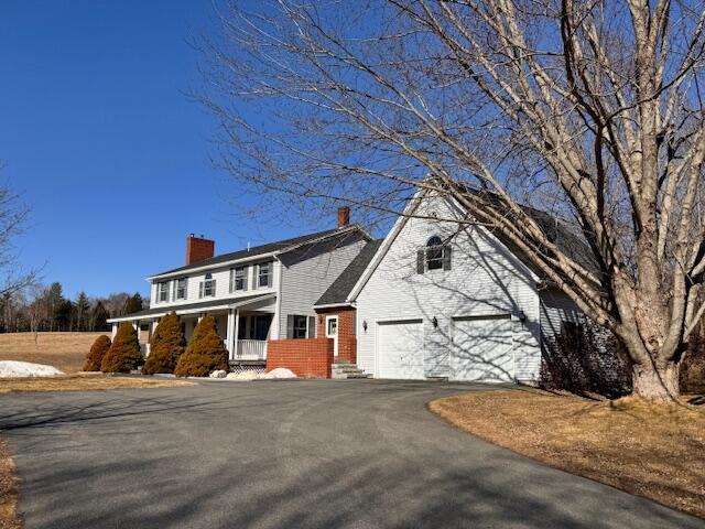 view of front of home with covered porch, a chimney, an attached garage, brick siding, and aphalt driveway