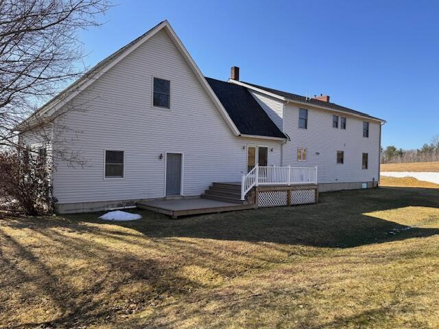 rear view of property featuring a lawn, a chimney, and a wooden deck