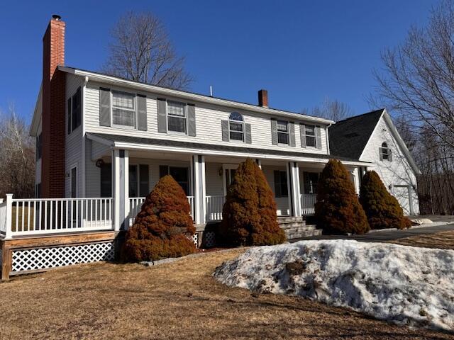 colonial-style house featuring a chimney and covered porch