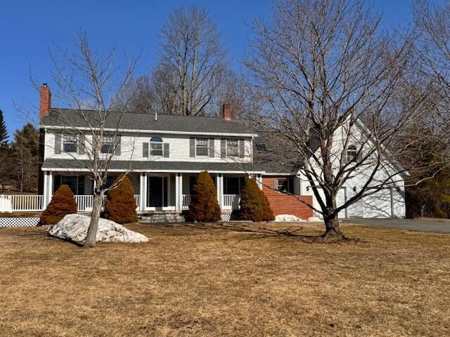 view of front facade with covered porch, a chimney, concrete driveway, and a front yard