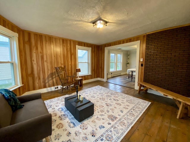 living area featuring a baseboard radiator, dark wood-style flooring, a textured ceiling, and wood walls